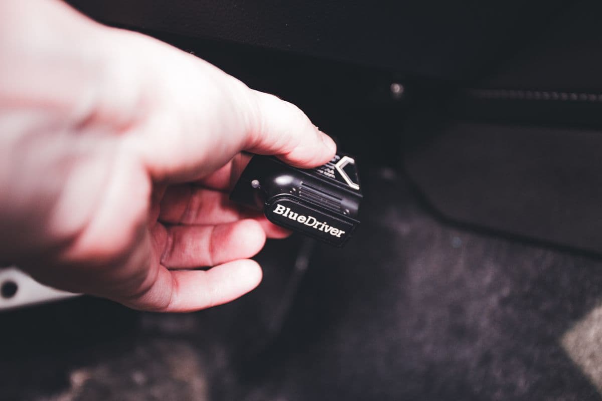 Main branchant un boîtier de diagnostic sur la prise OBD, sous le volant d'une voiture